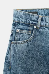 Jeans de tiro alto, estilo balloon leg, largo completo. Denim azul claro con efecto lavado ácido o 'acid wash'. Presenta cinco bolsillos y cierre frontal con cremallera y botón.