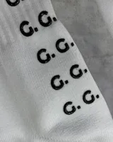 Par de medias deportivas blancas con texto 'GAINS.' en negro y agarre antideslizante con el logo 'G.G.' en la planta del pie.
