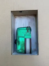 Billetera porta celular de cuero verde metalizado con correa de tela a rayas grises y marrones.