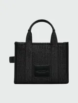 Bolso tote pequeño Marc Jacobs, tejido en color negro, con manijas cortas y correa larga ajustable. Estampado frontal con el texto "THE TOTE BAG MARC JACOBS" en color blanco.