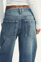 Pantalón de jean azul oscuro, tiro medio, corte amplio tipo baggy balloon con costuras torcidas y cinco bolsillos. Cierre frontal con cremallera y botón metálico.