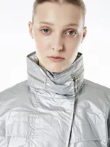 Campera plateada de poliéster con capucha ajustable y cintura con cordón ajustable interno. Cuenta con cierre frontal con botones a presión, bolsillos laterales con cierre y mangas 3/4 con puños elásticos.