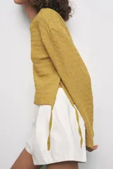 Top mostaza de cuello barco y manga larga con textura. Tiene lazadas ajustables en el bajo.