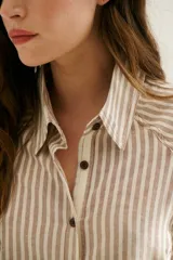 Camisa a rayas verticales color beige y blanco, con cuello clásico, botones marrones y mangas largas.