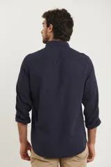 Camisa azul marino de lino y algodón, con cuello abotonado, manga larga con puños enrollados, bolsillo de parche en el pecho y cierre frontal con botones.