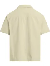 Camisa de manga corta color beige, confeccionada en algodón texturizado con bolso de parche y cierre frontal con botones.