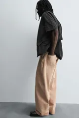 Pantalón de jean color beige, de corte ancho y tiro medio, con cinco bolsillos, efecto lavado y cierre frontal con cremallera y botón.