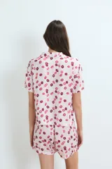 Pijama de dos piezas, compuesto por una camisa de manga corta con cuello y botones frontales, y un short. El conjunto es de color rosa pálido con un estampado repetitivo de labios en tonos rosados y burdeos.