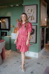 Vestido camisero corto color rosado, con cuello camisero, mangas cortas abullonadas con volados, falda con volados en capas y cinturón de lazo. Confeccionado en lino.