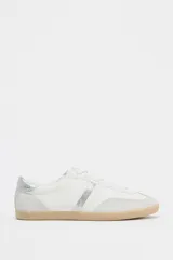 Zapatillas deportivas blancas con detalles plateados y suela color caramelo.