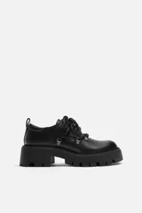 Zapato tipo derby de cuero negro con cordones y ganchos metálicos. Suela track con plataforma.