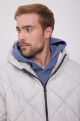 Campera puffer de hombre color gris claro, con capucha ajustable con cordón, cierre de cremallera frontal, bolsillos laterales y mangas largas. Tejido acolchado resistente al viento.