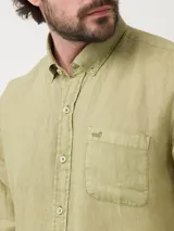 Camisa de lino color verde oliva, con cuello camisero, teñida en prenda. Tiene un bolsillo en el pecho con bordado al tono. De manga larga y calce regular.