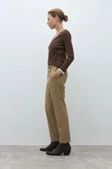 Pantalón negro de vestir, corte recto y tiro alto, con pliegues frontales y puños doblados. Se complementa con un cinturón fino negro con hebilla metálica en forma de símbolo.