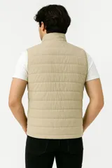 Chaleco acolchado color beige con cierre frontal y bolsillos laterales.