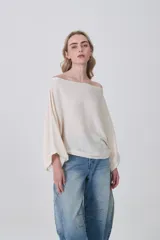 Sweater holgado de tejido ligero, color beige claro, con escote asimétrico que deja un hombro al descubierto.