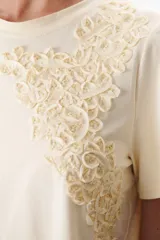 Remera blanca de manga corta con detalle de encaje floral en el hombro.
