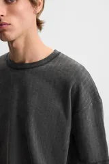 Camiseta color gris verdoso de punto tejido en hilatura de algodón, con cuello redondo, manga corta, efecto lavado y acabados irregulares.