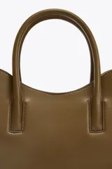 Bolso shopper de mano color marrón, con asa doble y correa bandolera extraíble. Tiene cierre imantado y un bolsillo interior con cremallera.