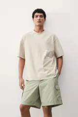 Short cargo color verde claro en popelina de algodón, con cintura elástica ajustable con cordón, bolsillos laterales, bolsillos cargo con solapa y botón a presión en piernas y traseros, y aberturas laterales en el bajo.