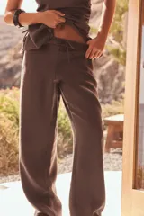 Pantalón marrón de tela fluida, corte recto, tiro medio y cintura elástica ajustable con cordones. Incluye bolsillos laterales ocultos en la costura.
