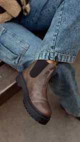 Bota Chelsea de cuero marrón con elásticos laterales negros, tiradores traseros y suela track negra.