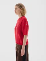 Remera de punto negra con cuello redondo y mangas cortas. Presenta un diseño de tejido con trenzas verticales.