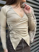 Blusa color beige con escote en V cruzado, mangas largas y detalle de hebilla metálica en el lateral.