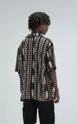 Camisa de manga corta tejida en punto abierto (símil crochet), con calce oversize. Presenta un patrón geométrico en tonos negro, marrón y blanco.