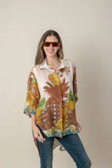 Camisa italiana de corte irregular con estampado de piñas, flores y animales en tonos marrón, amarillo, azul y verde sobre fondo natural.