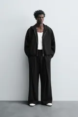 Pantalón jogger negro de corte relaxed fit, confeccionado en tejido de algodón. Presenta cintura elástica ajustable con cordón, pliegues frontales, bolsillos delanteros y un bolsillo trasero.