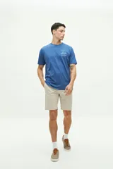 Remera azul de manga corta con cuello redondo y estampado de playa con sombrilla, reposera, balde y pala.