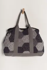 Bolso tipo tote amplio, confeccionado en patchwork de hexágonos con diferentes estampados en tonos azul marino y blanco/gris. Presenta asas y base en tela lisa gris. El cuerpo del bolso tiene un efecto acolchado.