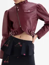 Chaqueta crop de cuero ovino color bordó, estilo biker, con cuello alto con volados y cierre metálico asimétrico. Presenta detalles de frunces en la copa de las mangas y volados en los puños.