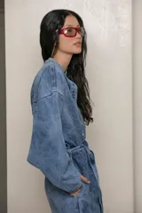 Mameluco de jean celeste con efecto nevado vintage, corte holgado, cuello mao, cierre frontal con botones y cinturón de lazo.