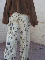 Pantalón de jean recto y ancho, de tiro medio, con estampado de manchas irregulares en tonos beige y gris oscuro.