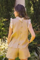 Blusa de lino color blanco, sin mangas, con cuello fruncido y volados de encaje en las sisas. Presenta pinzas frontales y un diseño de calce holgado de estilo romántico.