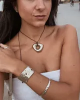 Collar con dije dorado irregular con agujero central, colgando de cordón negro ajustable.