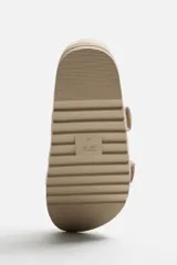 Sandalias planas color beige con doble tira ancha en el empeine y cierre con hebilla.