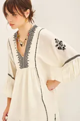 Vestido corto negro con bordado de hilo blanco, escote en V y mangas largas abullonadas.