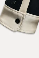 Camisa negra de terciopelo con cuello solapa, manga larga con puños en tejido color crema a contraste y bajo redondeado.