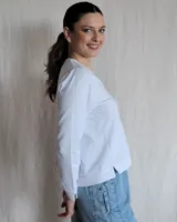Remera blanca de mangas largas con cuello en V y costuras a la vista.