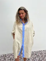 Vestido camisero beige de lino con cuello y solapa azul lavanda, cierre frontal con botones y mangas largas.