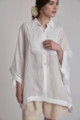 Camisa blanca de lino con cuello clásico, cierre frontal con botones y mangas anchas 3/4. Presenta detalles de bordado calado en el frente y puños.