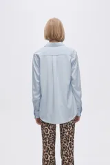 Camisa blanca de manga larga con cuello clásico y cierre frontal con botones. Corte recto y holgado.