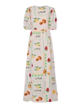 Vestido largo confeccionado en una mezcla de viscosa, algodón y lino con estampado de frutas y soles sobre un fondo rosado pálido. Presenta cuello en V, mangas de largo medio con puños elásticos y un cierre frontal completo con botones.