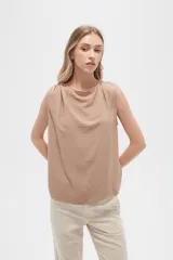 Blusa color beige de poliéster, sin mangas, con cuello asimétrico y detalle de drapeado en los hombros.
