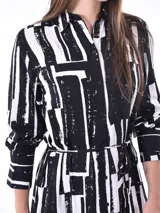 Vestido midi estampado en blanco y negro, con cuello mao y cierre frontal parcial. Presenta mangas largas y un cinturón fino a juego que ajusta la cintura.