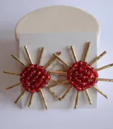 Par de aros colgantes con cuentas rojas y apliques dorados en forma de rayos.