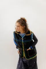 Chaleco negro de corderito con cierre de alamares y tejido a mano en crochet con detalles en amarillo, verde, celeste y azul.